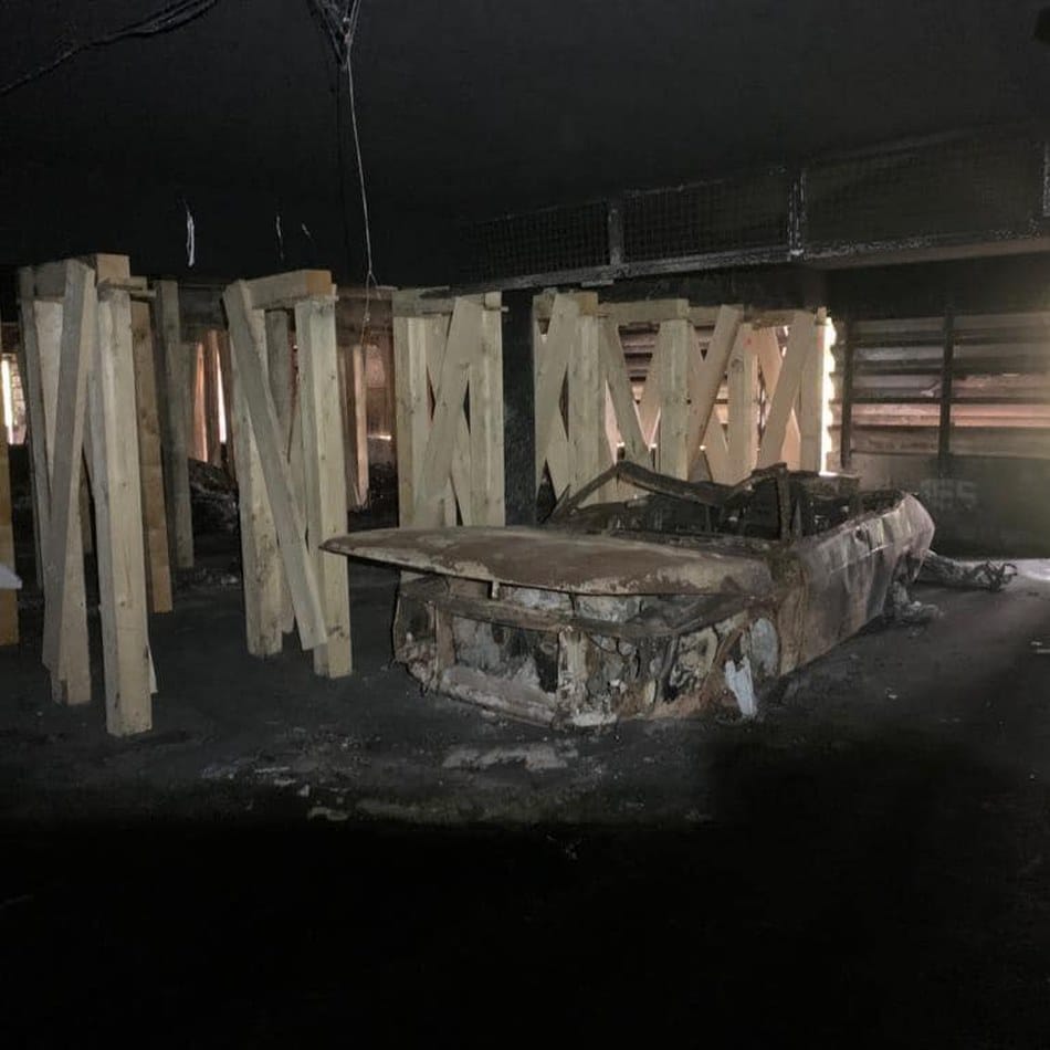 Ausgebranntes Fahrzeugwrack in einer Tiefgarage, deren Decke nach dem Brand mit Holzstützen gesichert wurde