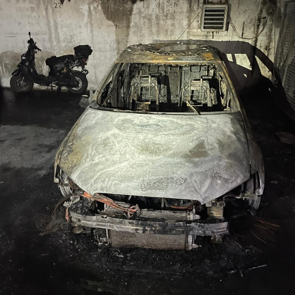Vollständig ausgebranntes Auto in einer verrußten Tiefgarage, Frontansicht mit zerstörtem Innenraum und freiliegenden Sitzgestellen
